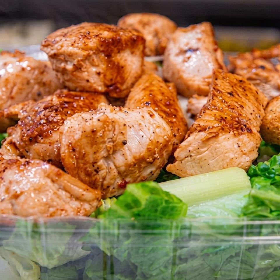 Seasoned roasted chicken pieces piled over crisp lettuce and cucumber in a clear serving dish.