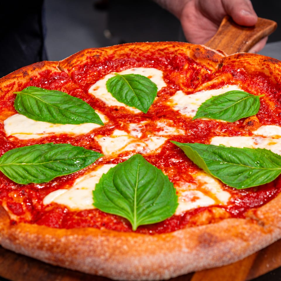 Margherita pizza with tomato sauce, melted mozzarella, fresh basil leaves, and a thick charred crust on a wooden serving board.