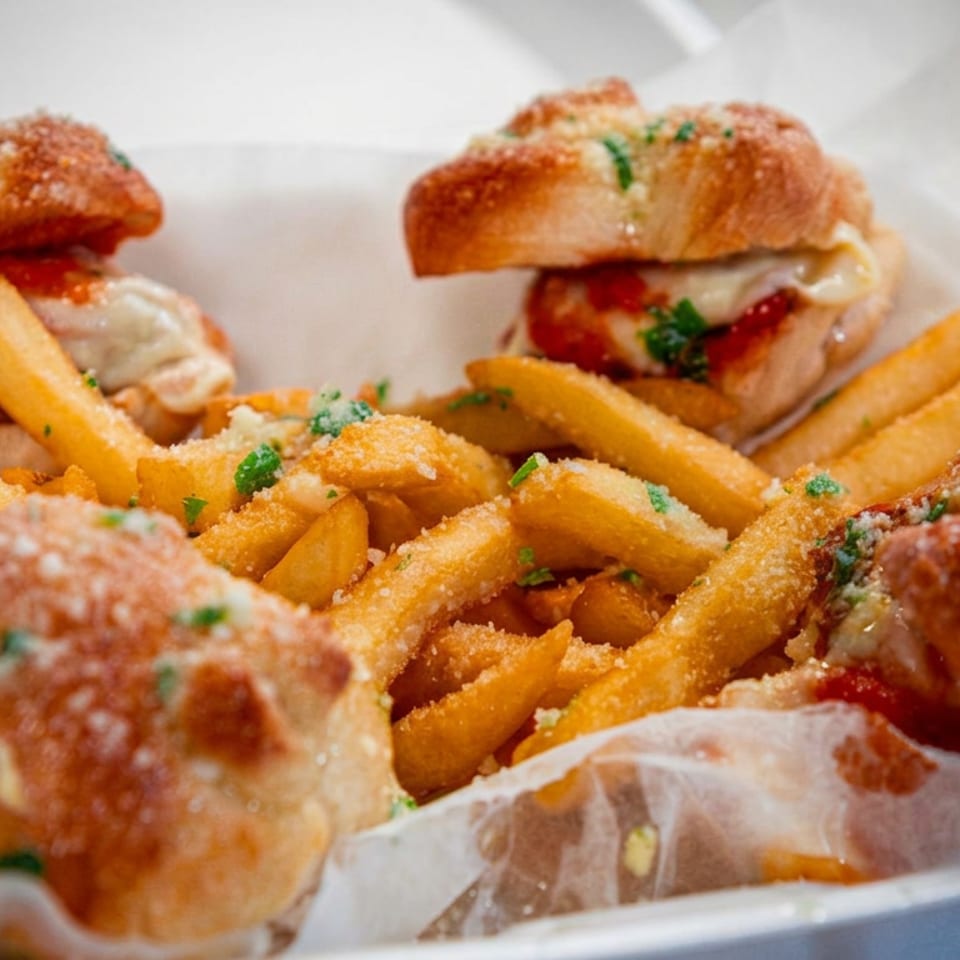Tray of mini meatball sandwiches with melted cheese, marinara sauce, fries, grated cheese, and parsley.